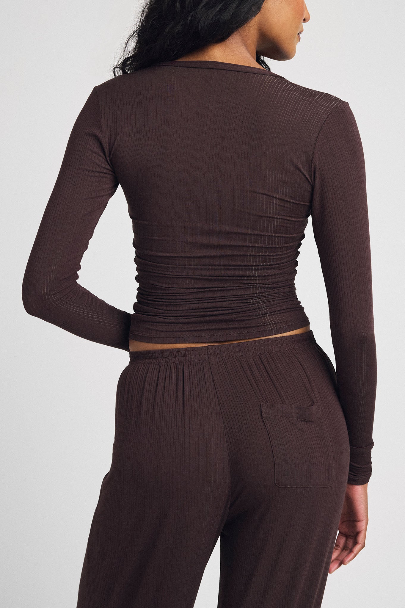 Back view of ribbed long-sleeve henley romper with ruched waist and dark brown shorts